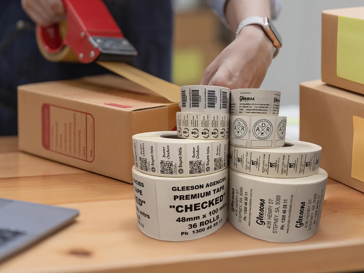 Stack of label rolls on a table with person packaging product