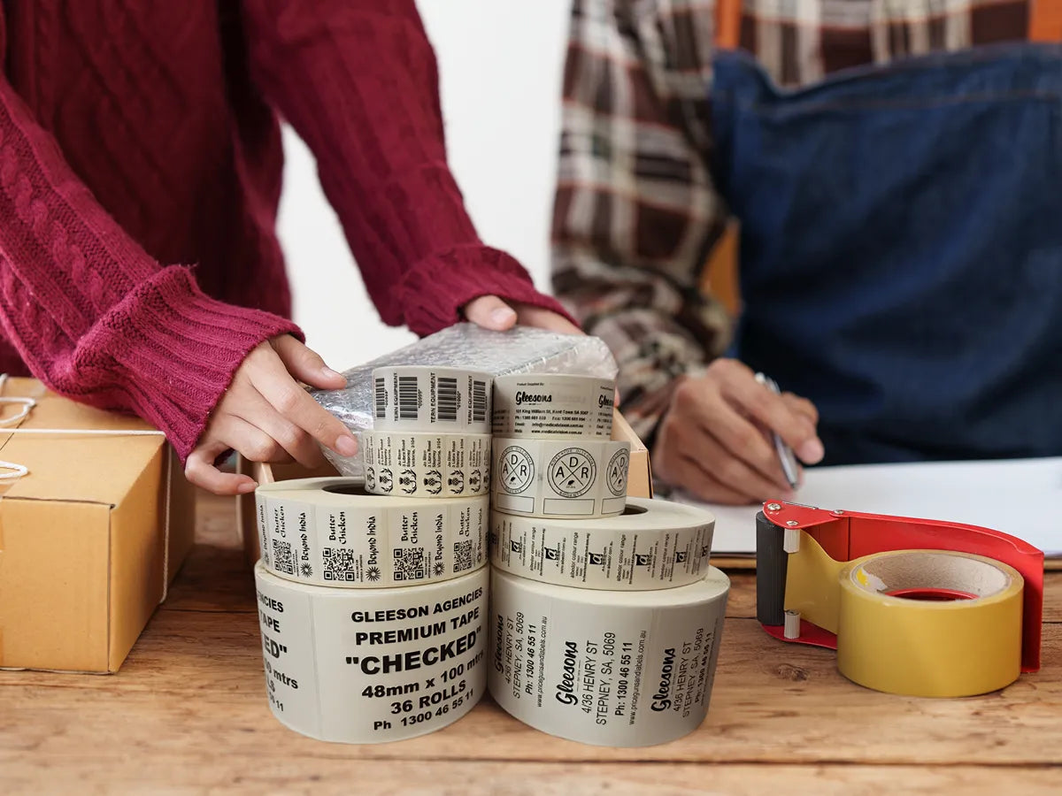 A stack of label rolls on a table with people handling product.